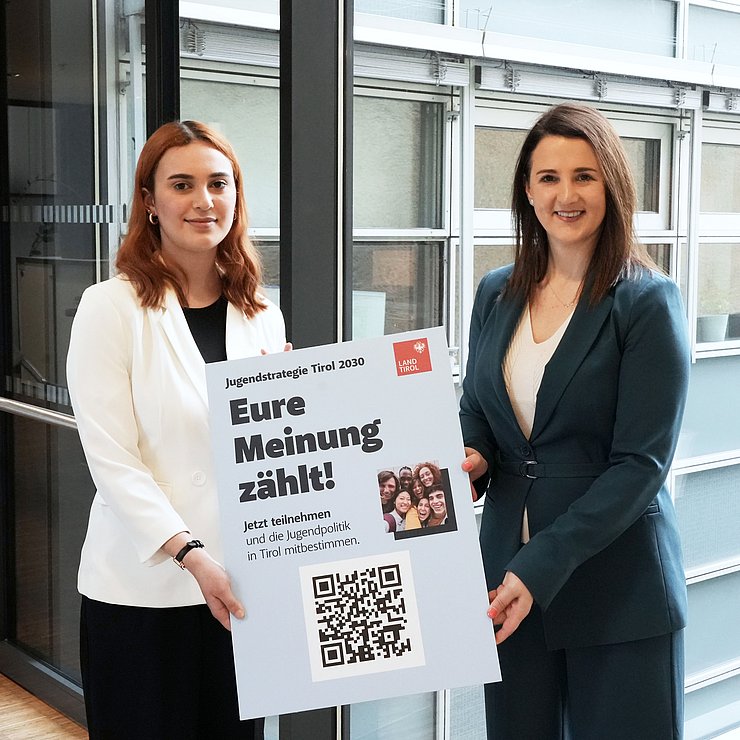 Mair und Gruber mit Tafel auf der ein QR-Code ist und der Text "Eure Meinung zählt"